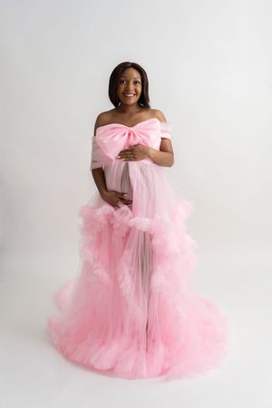 A maternity photoshoot featuring a pink tulle gown against a white backdrop.