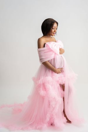 Elegant maternity photography session with soft pink tulle fabric in a minimalist studio.