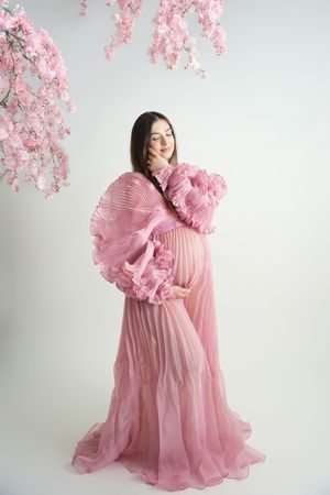 A dreamy pink fashion photo series featuring a flowing ruffled gown and cherry blossoms against a light backdrop.