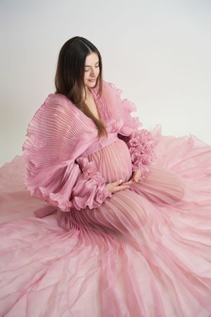 A dreamy portrait series featuring a flowing pink pleated gown against a white backdrop.