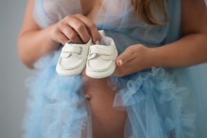 Small white baby shoes being held against a backdrop of light blue tulle fabric.
