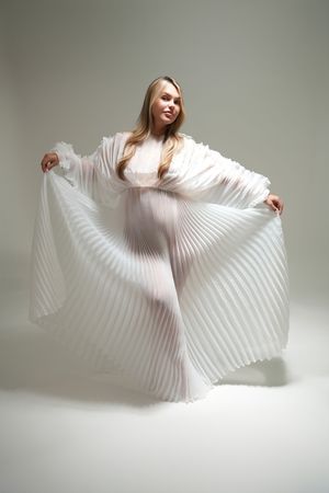A dancer in white clothing performs an elegant flowing movement sequence with billowing pleated fabric.