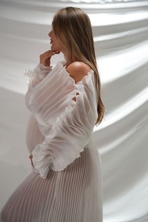 A person in soft light wearing a white ruffled blouse poses against draped white fabric backdrop in a series of photos.