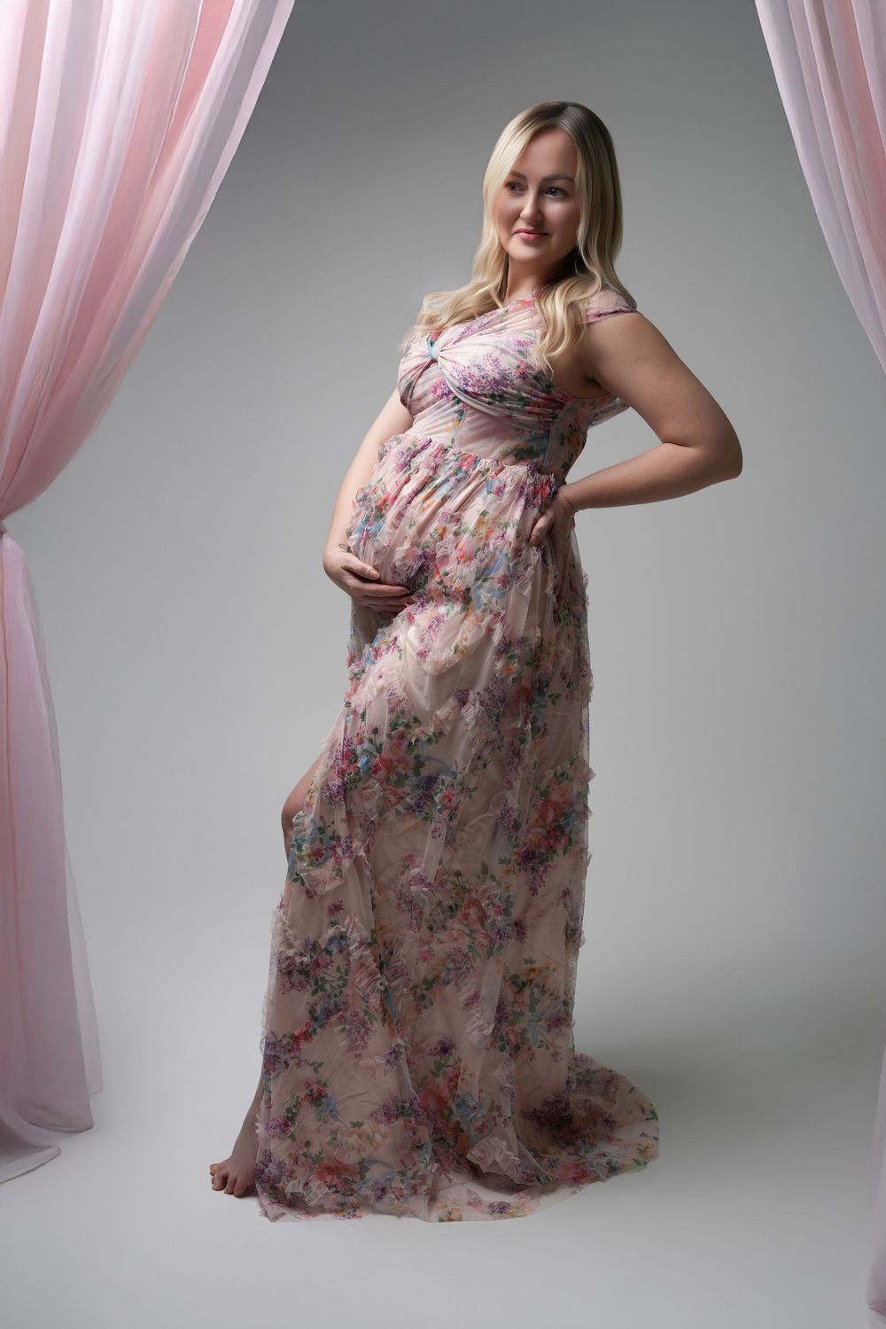 Maternity photoshoot showing a floral chiffon dress with flowing fabric against a pink curtained backdrop.