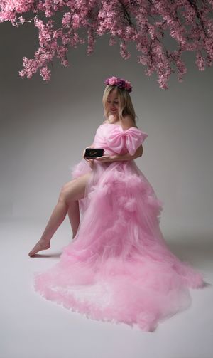 A dreamy portrait of someone wearing a flowing pink tulle gown and floral crown under cherry blossoms.