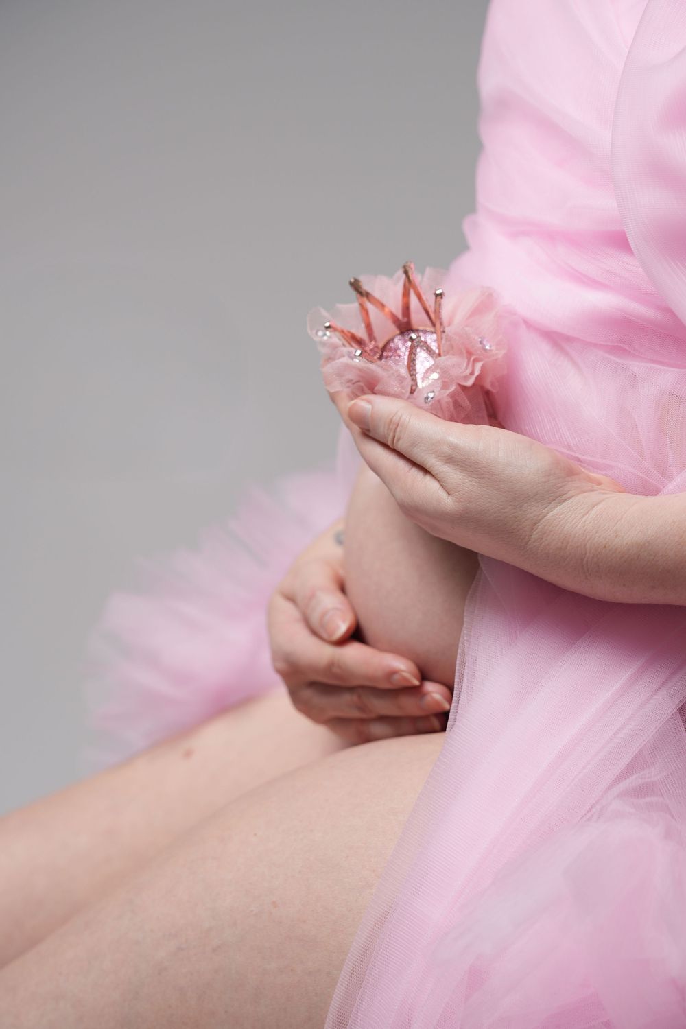 Hands delicately holding sheer pink fabric against a gray background in an artistic composition.