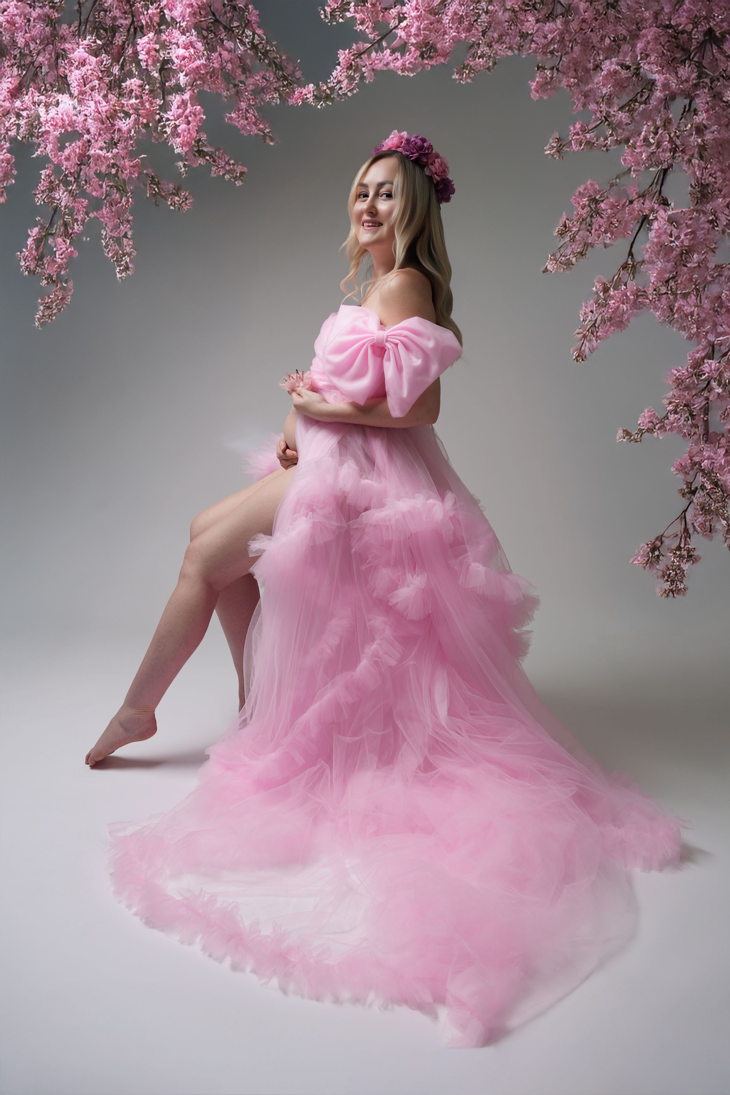 Ethereal pink dress flowing gracefully beneath blooming cherry blossom branches in a studio setting.