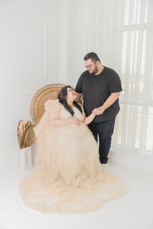 Romantic maternity session on wicker chair with flowing champagne tulle fabric.