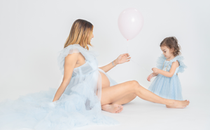 Artistic maternity poses with flowing light blue fabric in a minimalist studio setting.