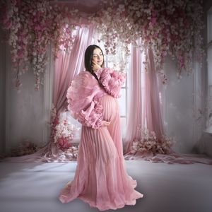 A dreamy pink maternity photoshoot scene with floral decorations and flowing fabric in a romantic studio setting.