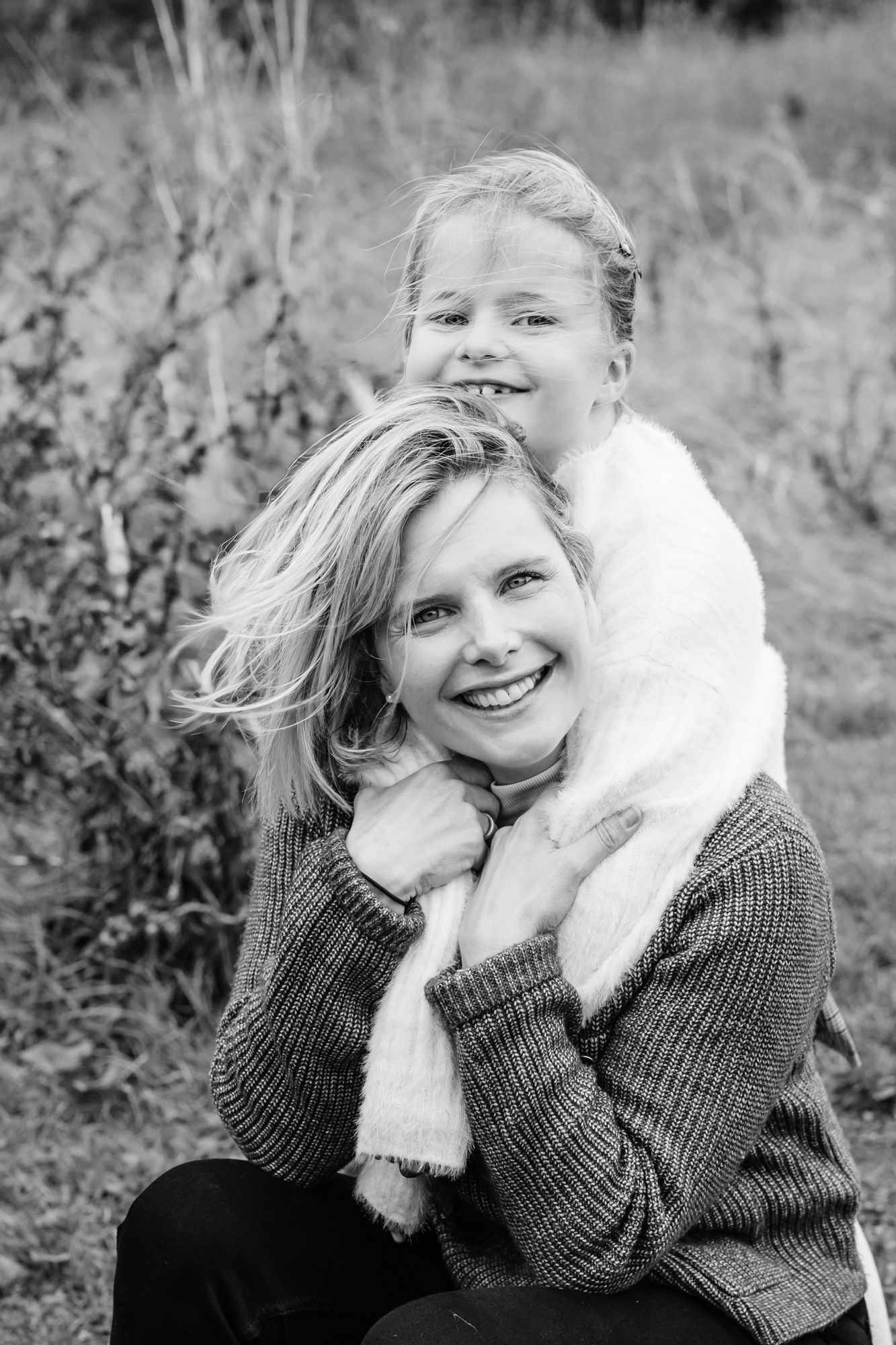 A series of black and white photos showing someone in a knit sweater cuddling with a white fluffy dog outdoors.