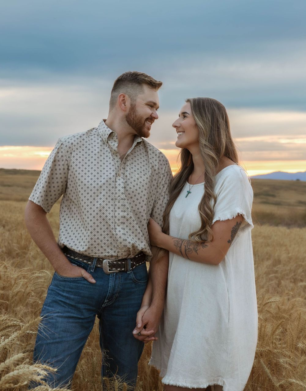 Playful couple photos captured in a wheat field with dramatic sky backdrop.