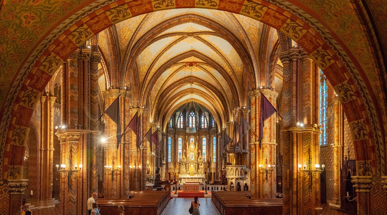 Panoramic view of a Gothic cathedral interior with ornate stone arches, stained glass windows, and warm lighting.