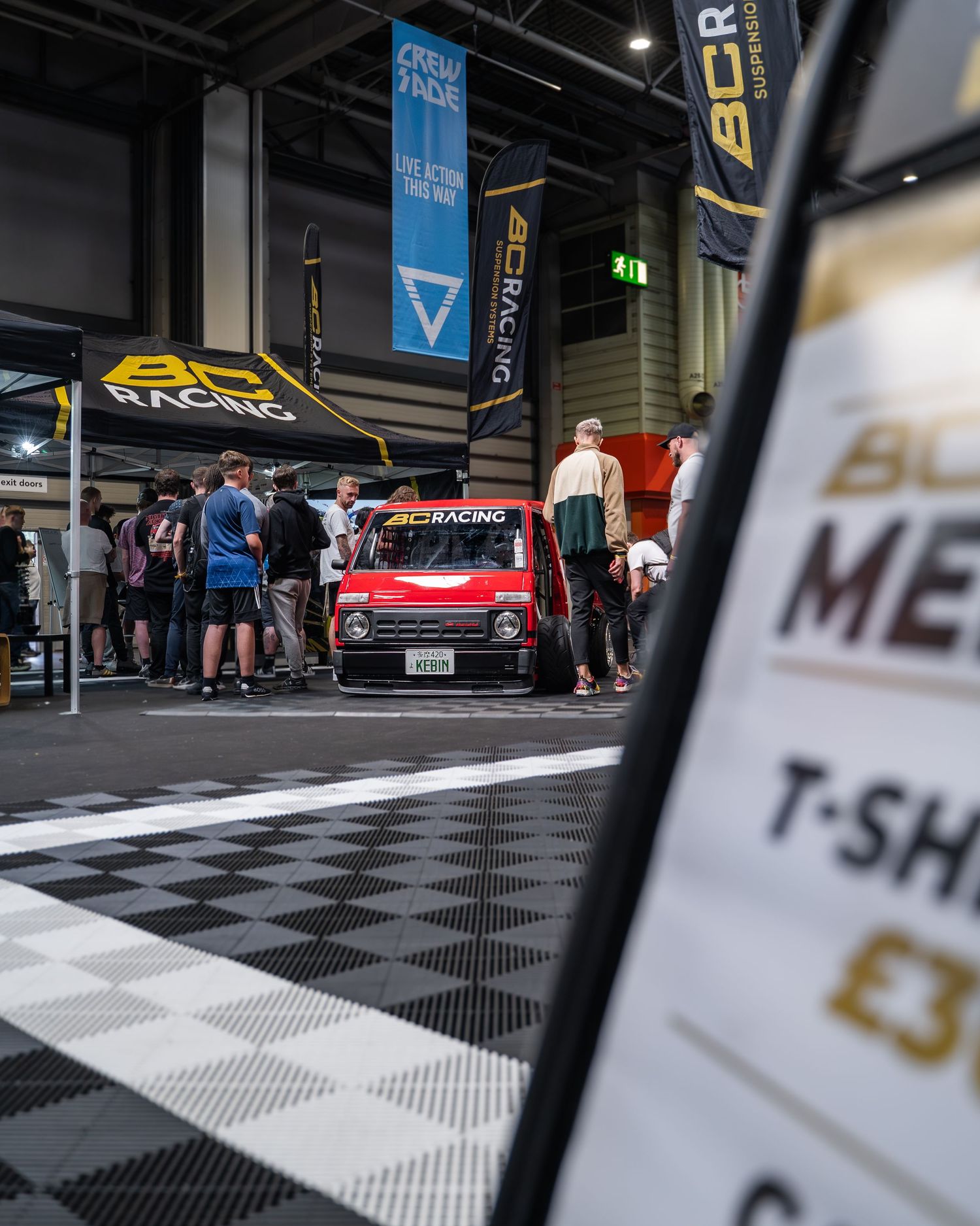 Car show floor with checkered tiles and display vehicles visible in exhibition hall.