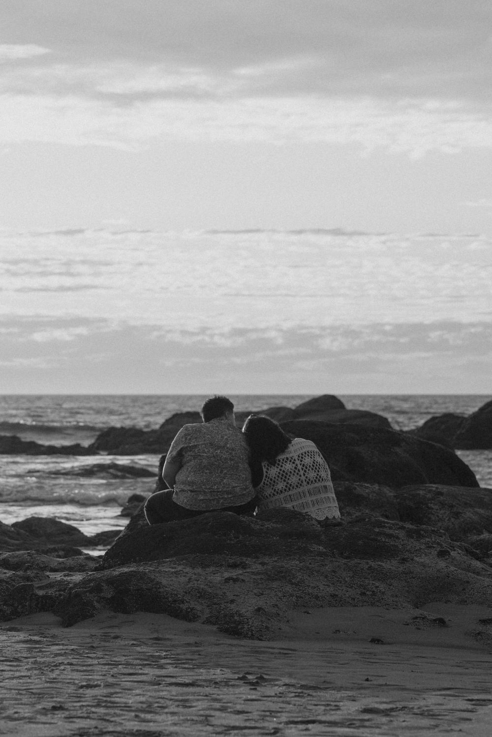 Silhouettes against a moody seascape with dark rocks and cloudy skies.