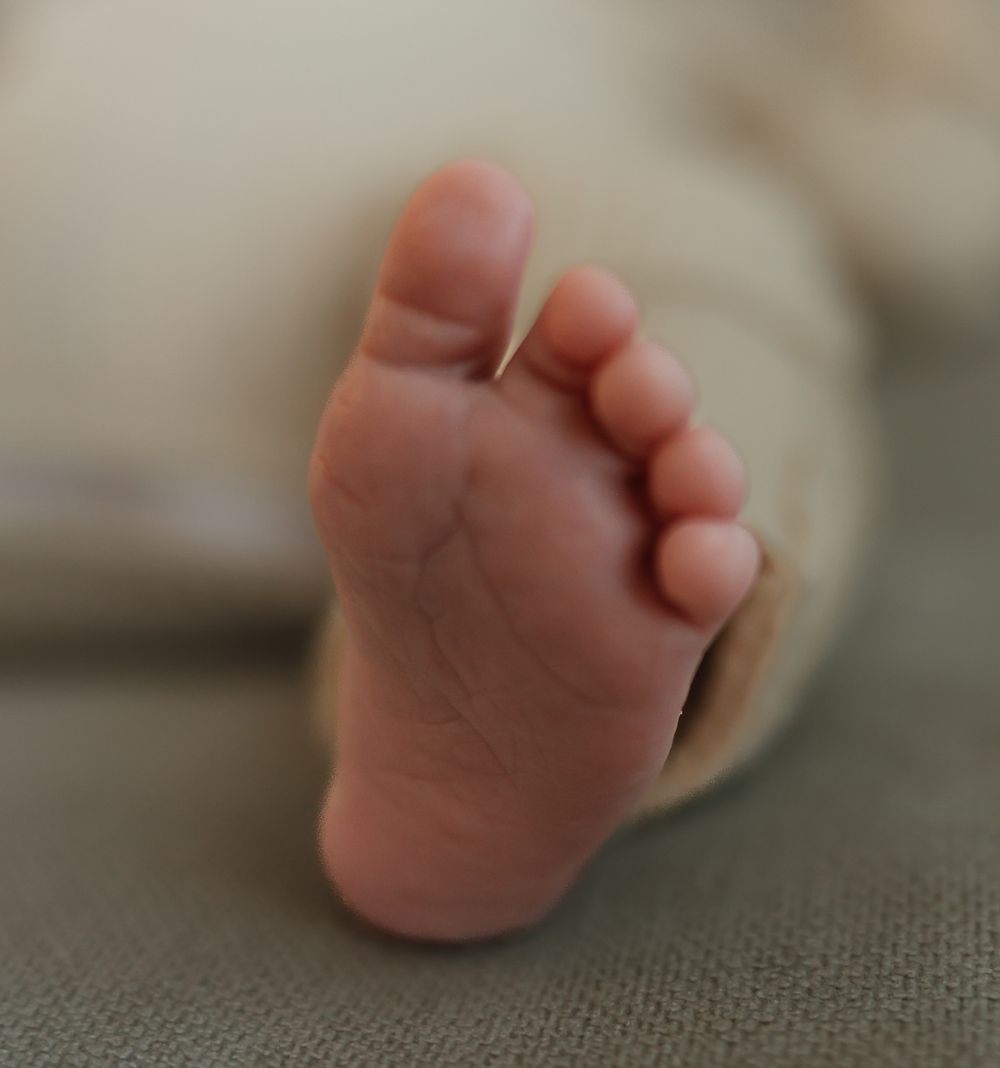 Close-up photo of a tiny baby foot on a textured gray fabric surface.