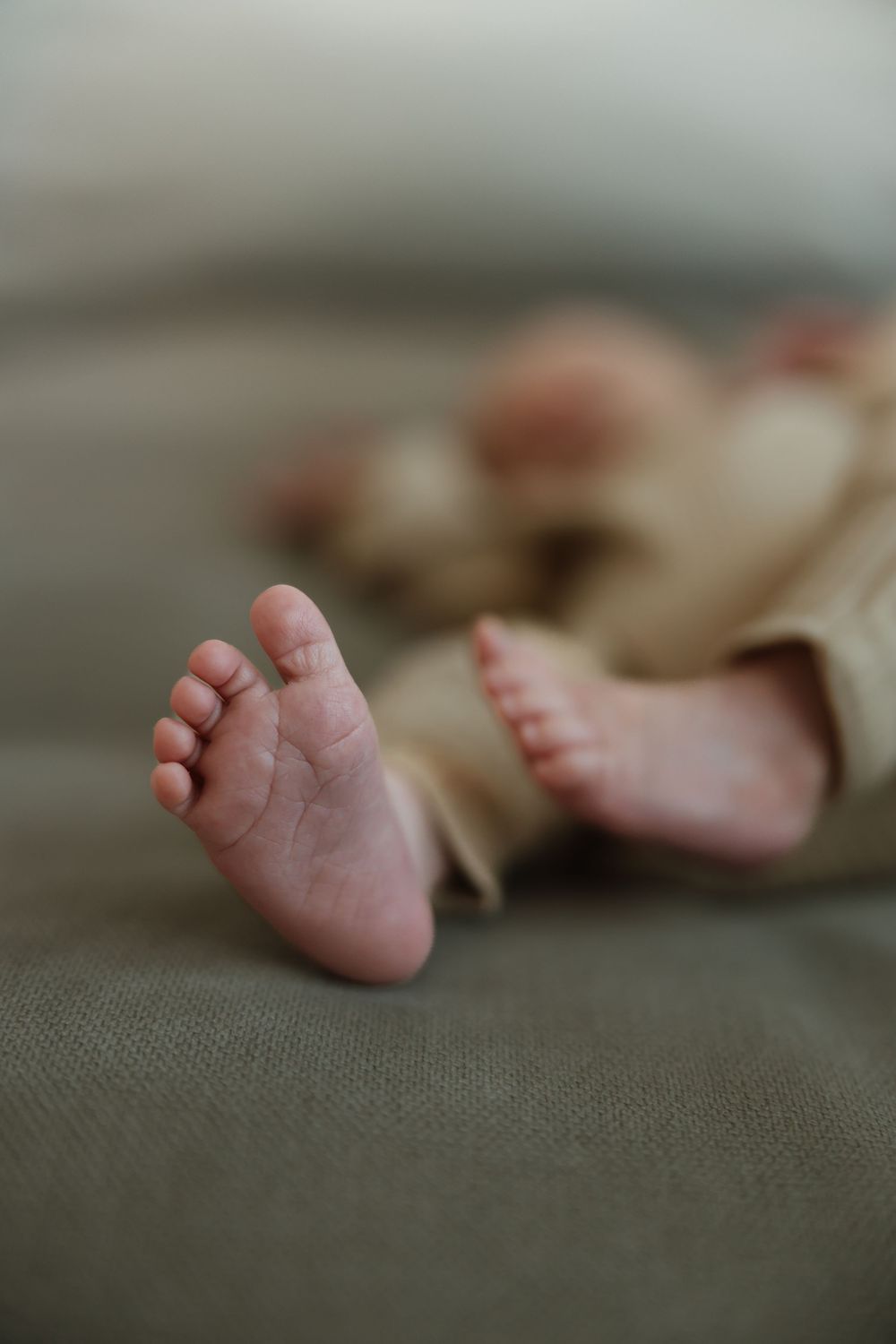 Tiny baby feet rest on a textured gray fabric surface in soft focus.