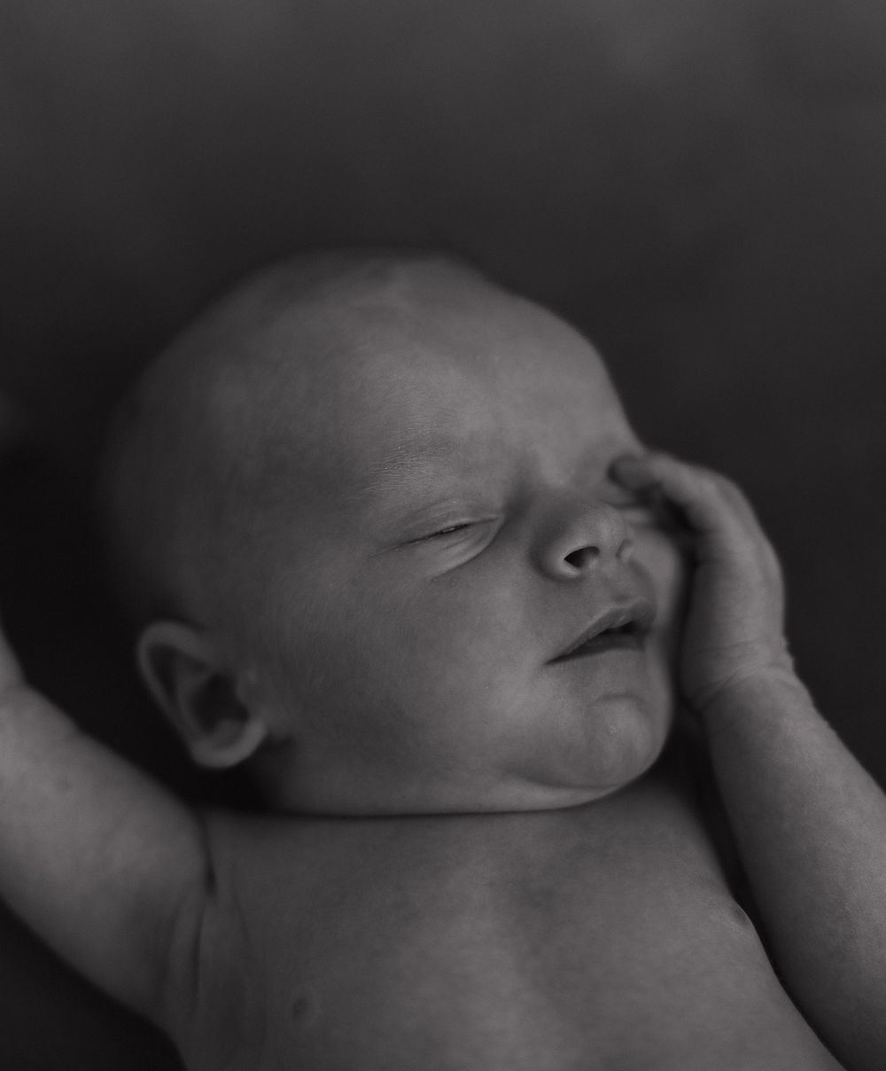 Black and white portrait of a peaceful sleeping newborn in dramatic lighting.