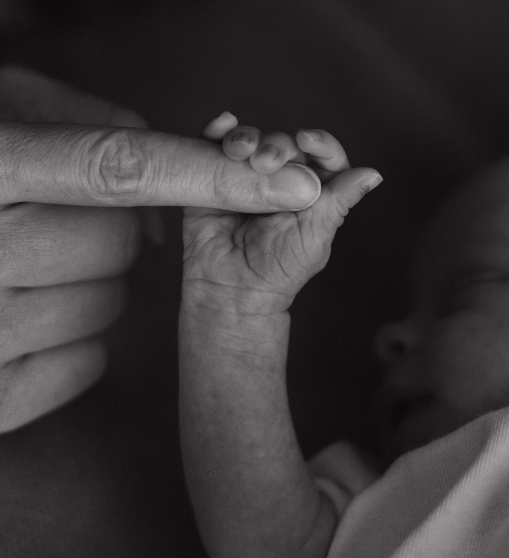 A close-up black and white image of small fingers grasping an adult's hand.