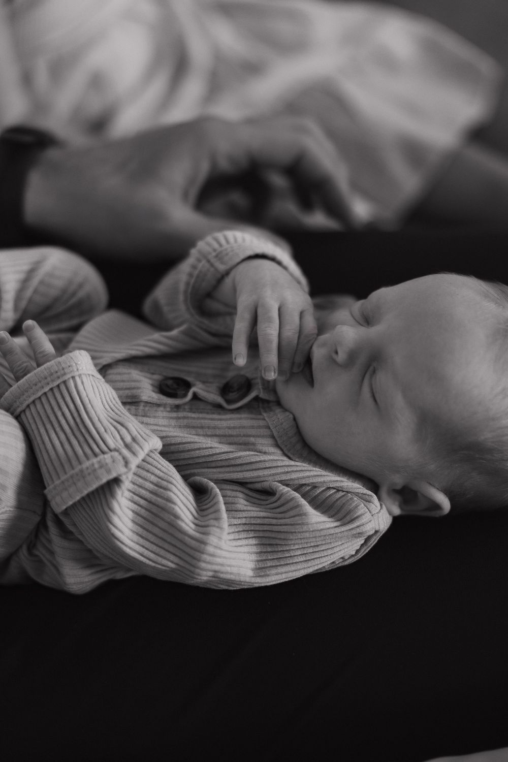 A sleeping infant wearing a ribbed sweater lies peacefully in black and white tones.