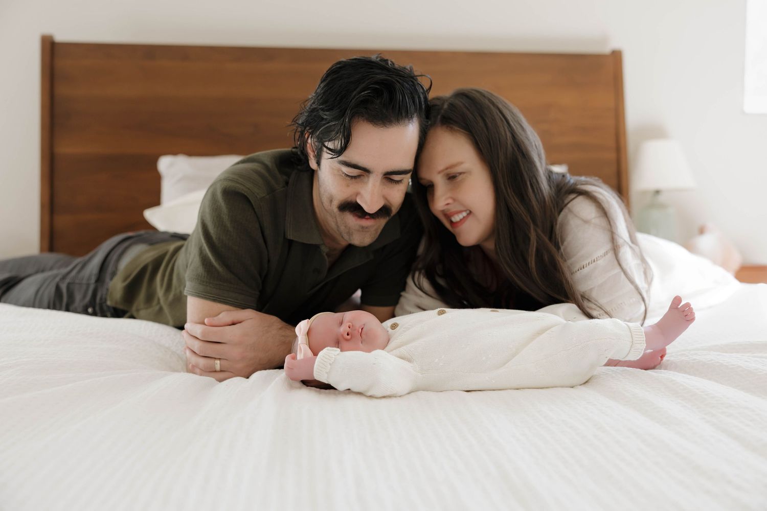 Happy couple lying together on white bed sheets while looking down at something with joy.