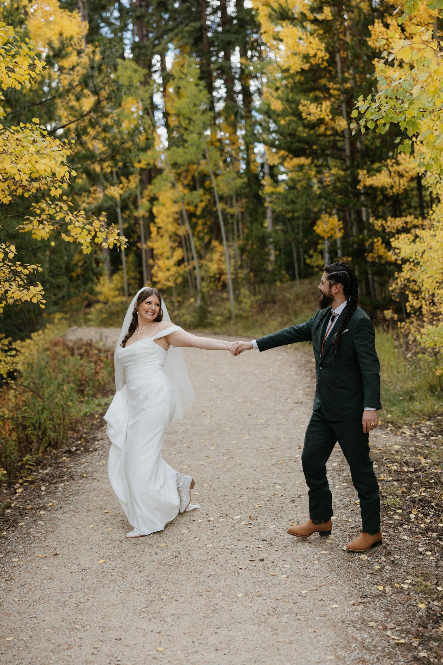 A couple in wedding attire playfully poses on a mountain trail surrounded by golden autumn aspen trees.