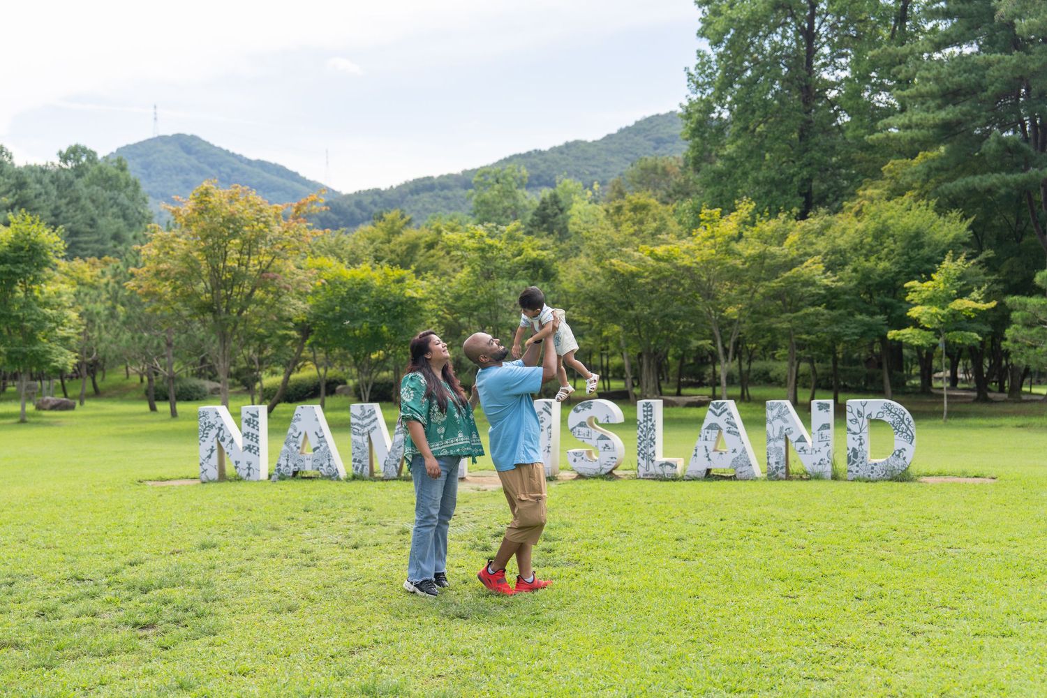 People pose together on a grassy lawn in front of large decorative letters spelling NAMI ISLAND in a mountain setting.