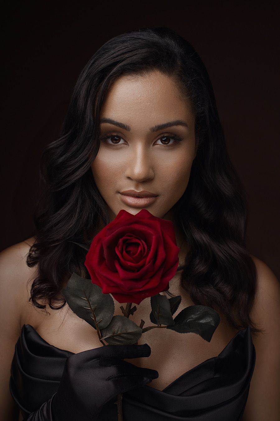 Valentine's Day. A glamorous portrait series featuring dark wavy hair and a red rose against a dark background.