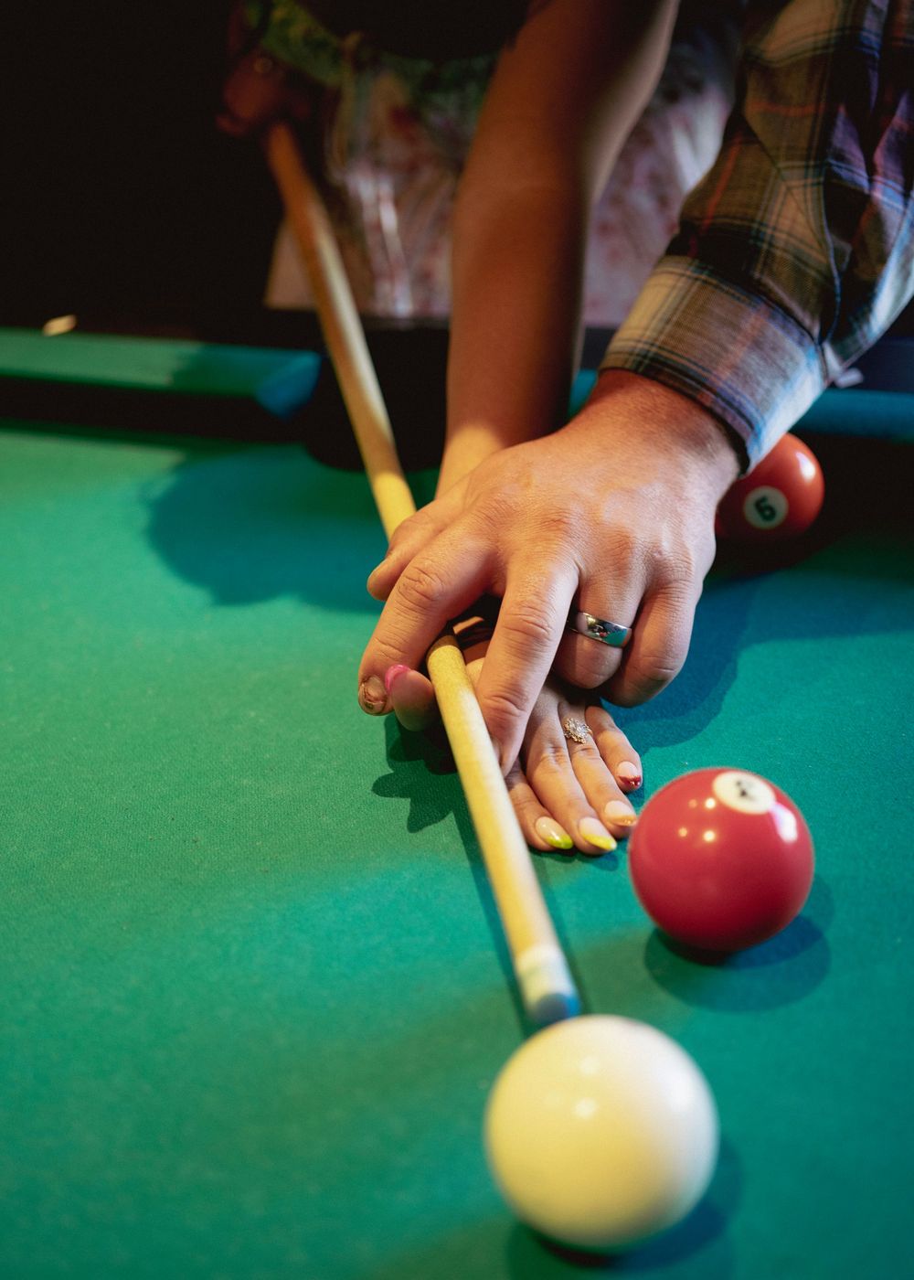 Close-up of hands playing pool, lining up a cue shot on a green billiard table with red and white balls.
