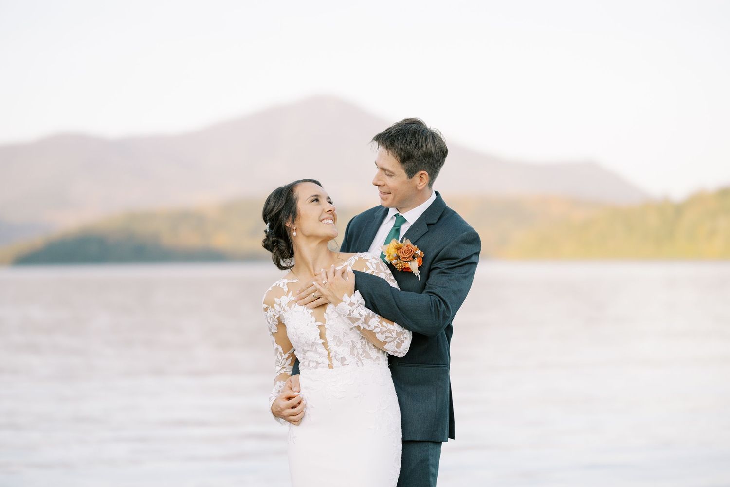 A romantic couple in wedding attire dances together against a scenic Adirondack mountain and Lake Placid landscape at sunset.