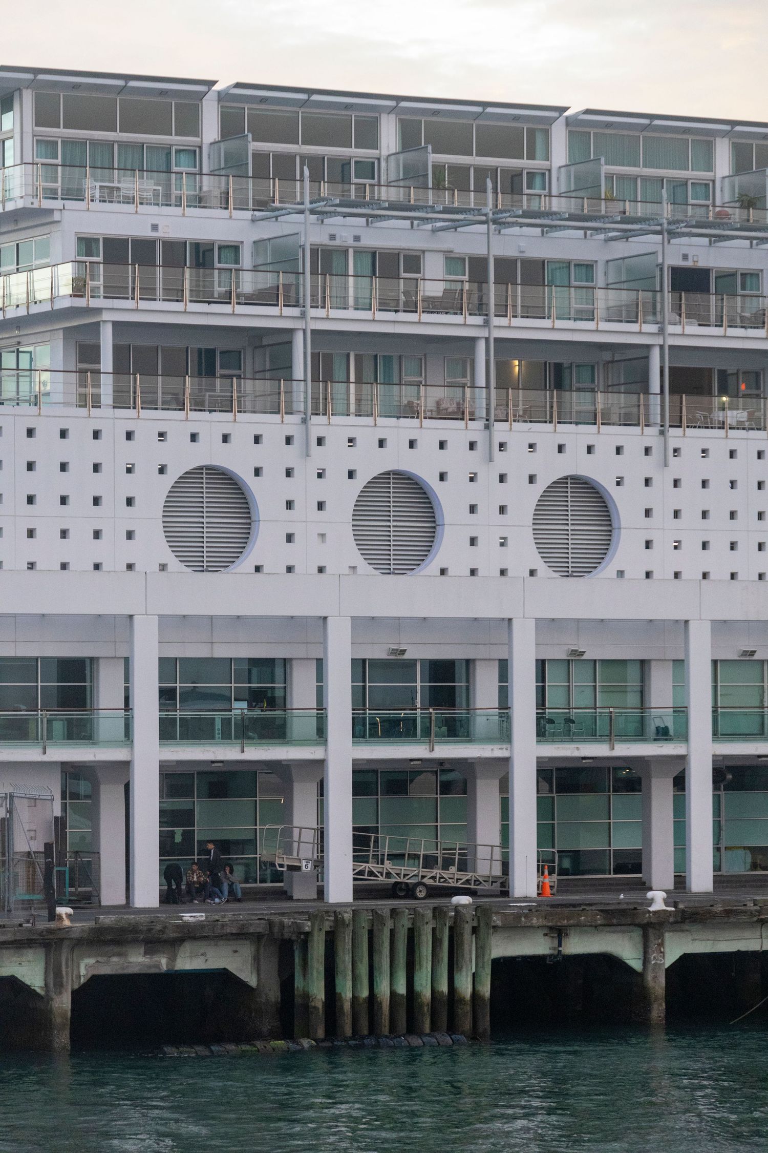 White modern apartment block with round porthole windows and balconies rises from the waterfront pier.