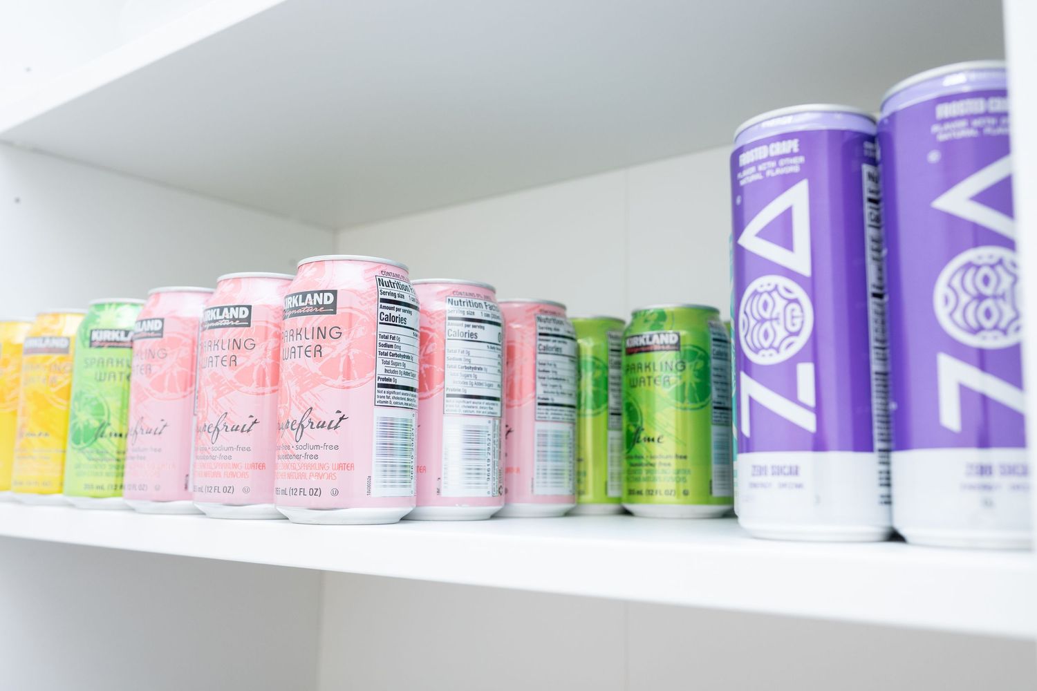 Colorful array of sparkling beverage cans neatly arranged on white shelf.