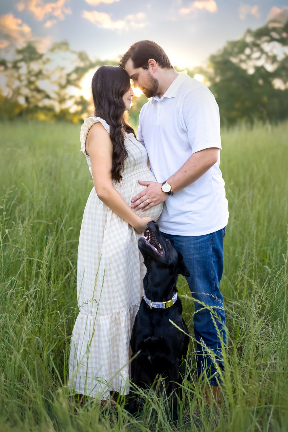 Expecting couple standing in tall grass with head touching each other with their black lab at golden hour in Watkinsville GA