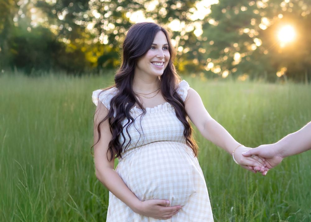 Couple holding hands in tall grass at sunset during their maternity photography session near Athens GA. You can only see the mother-to-be.