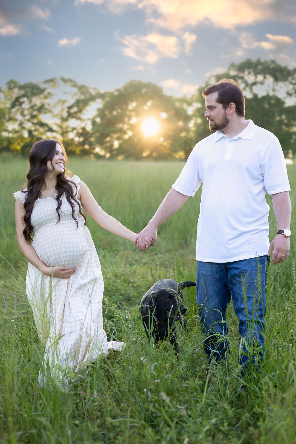 Couple holding hands in tall grass with sunset in the back during their maternity photography session near Athens GA