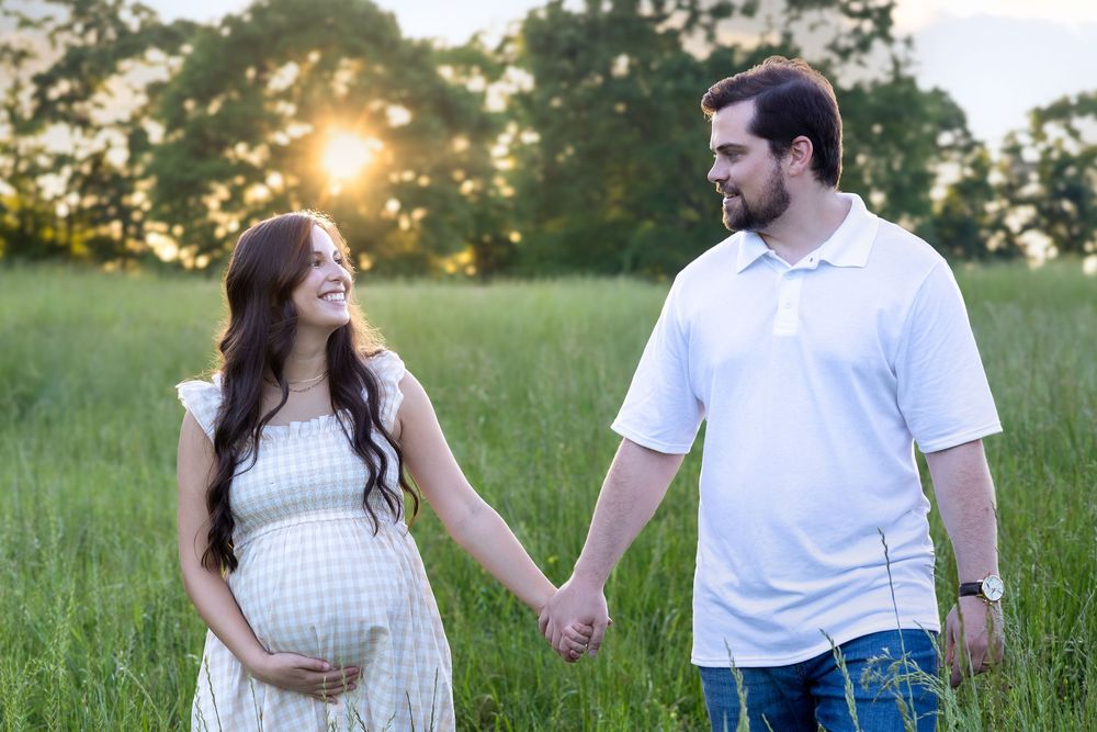 Couple holding hands in tall grass at sunset during their maternity photography session near Athens GA