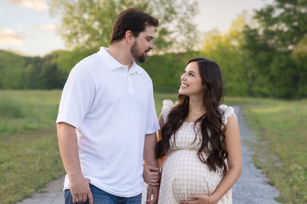 Golden hour maternity photo of couple holding belly and smiling on gravel path near Athens GA