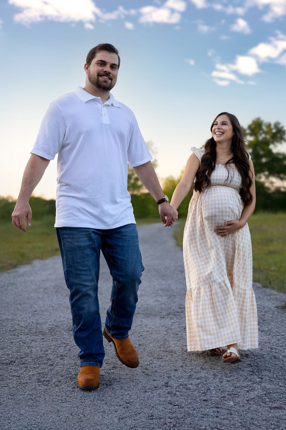 Golden hour maternity photo of couple holding belly and walking on a gravel path near Athens GA