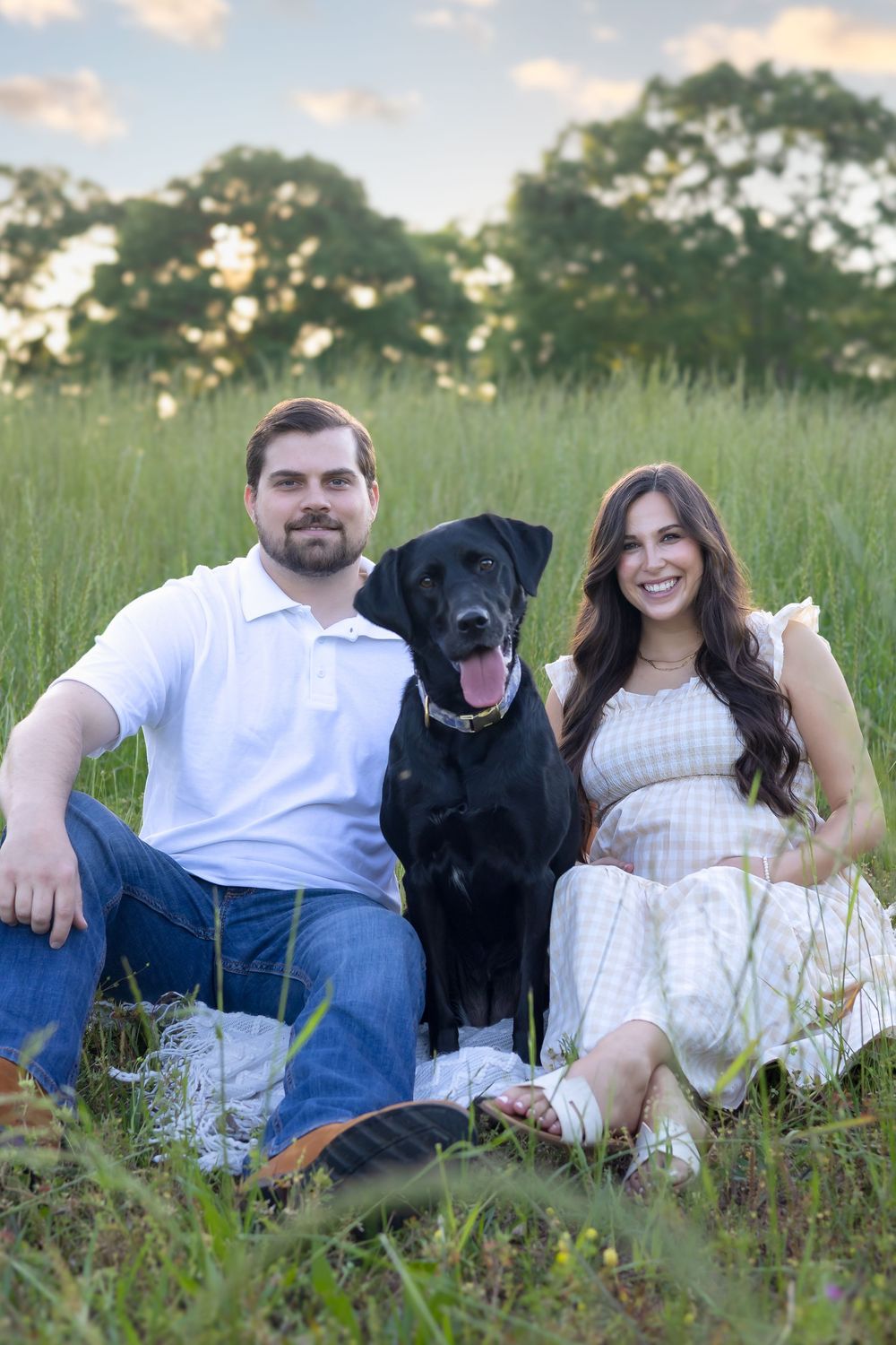 Pregnant couple holding belly and smiling at sunset in field of tall grass near Athens Georgia