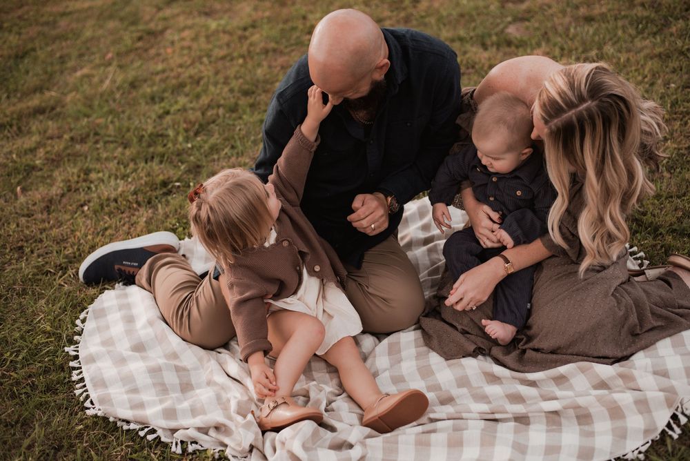 A family of four on a blanket in a field.