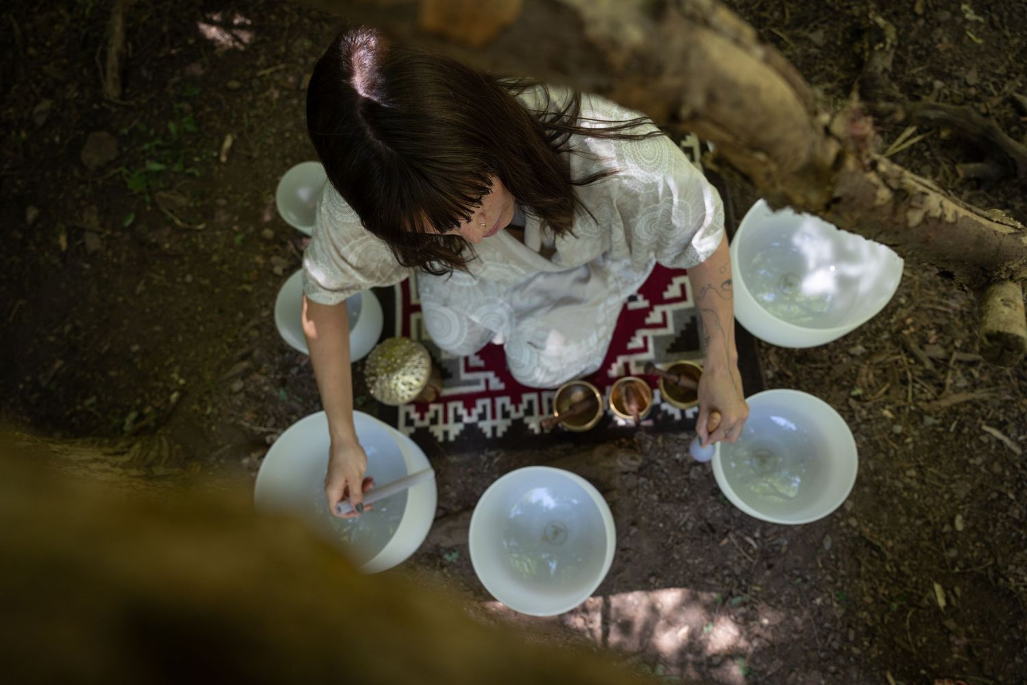 A woman playing crystal singing bowls in the forest.