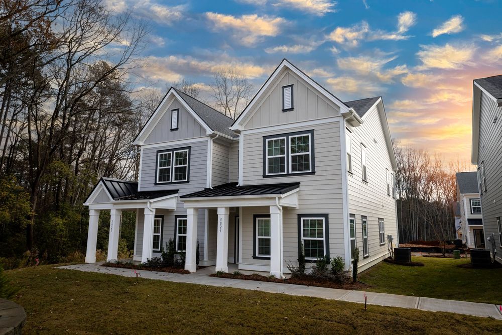Modern farmhouse style home with white siding, black windows and covered front porch at sunset.