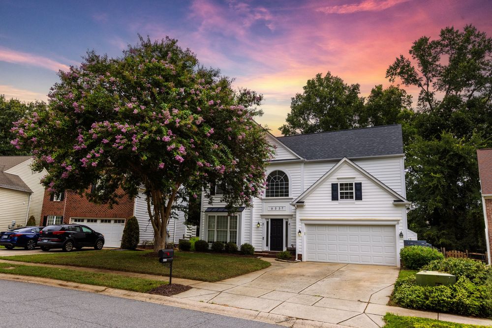 A row of suburban houses with white exteriors and attached garages under a colorful sunset sky.