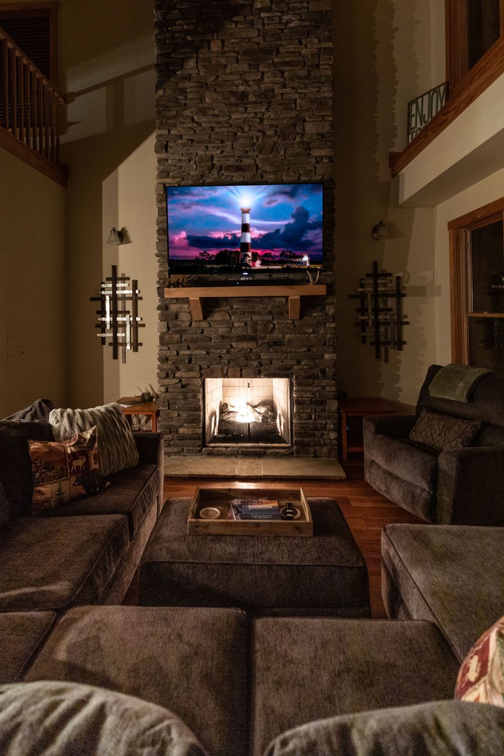 Cozy living area with stone fireplace and dark sectional sofa illuminated by warm lighting.