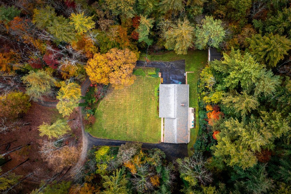 Aerial drone view of colorful autumn trees surrounding a white building in a lush forest landscape.