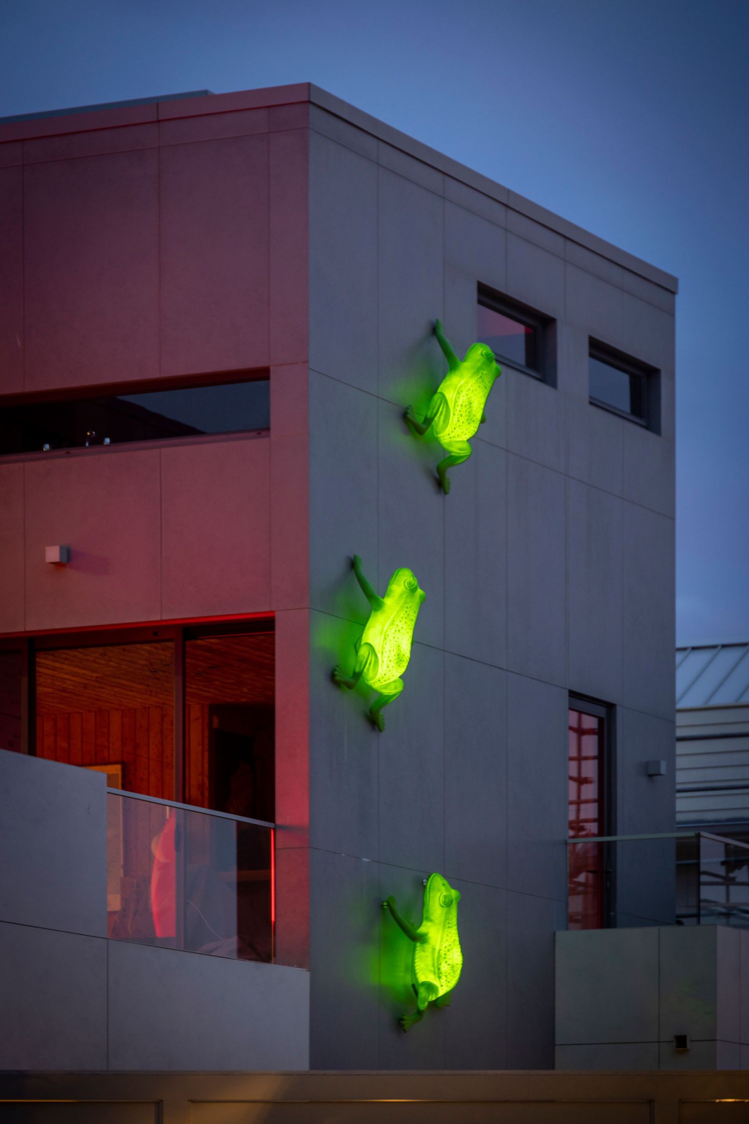 Neon green sculpture installation on concrete building glowing at dusk.