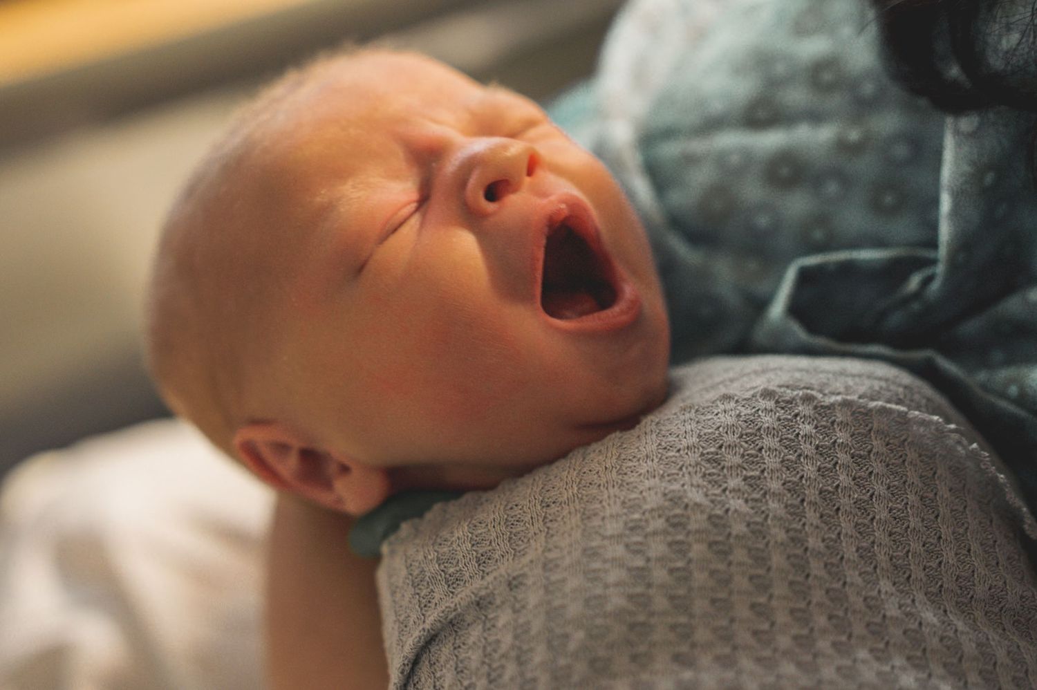 Close-up of baby sleeping peacefully on textured gray blanket.