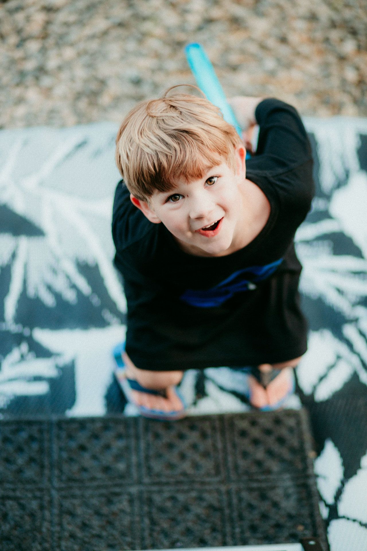 High angle view of a young person in a black sweater lying on a patterned surface looking up with an expressive smile.