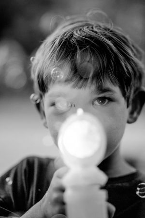 A black and white portrait of a child blowing bubbles outdoors.