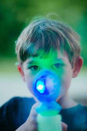 A child playing with a glowing blue light-up toy that illuminates their face against a blurred green background.